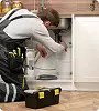 loodgieter die leidingen onder de keukenwasbak repareert met een gereedschapskist in de buurt, die woningreparatie, loodgietersonderhoud en residentiële servicewerkzaamheden vertegenwoordigt